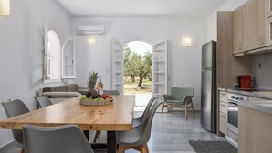 Eine moderne Küche mit einem Holztisch, grauen Stühlen und Blick auf einen Garten durch offene Türen.