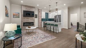 Una sala de estar moderna con chimenea, una zona de comedor y una cocina con taburetes de bar.