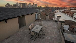 Una terrazza sul tetto con tavolo e sedie, uno skyline urbano sullo sfondo e un edificio in mattoni alla destra.