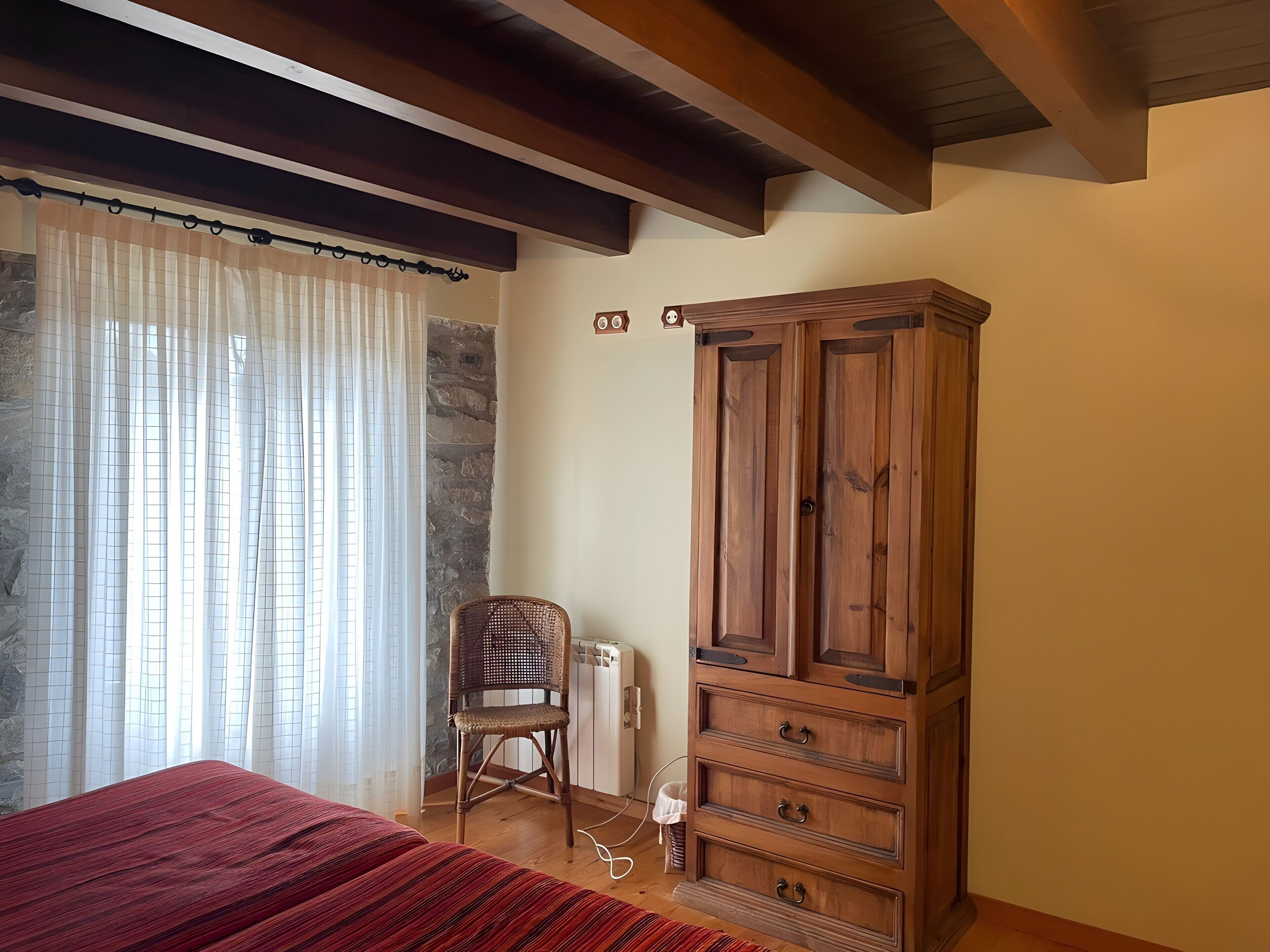 Ein Zimmer mit einem Bett, einem Holzschrank, einem Korbstuhl und einer Steinwand.