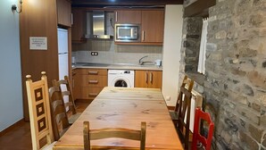 Cocina compacta con muebles de madera, microondas, lavadora y comedor con mesa y sillas de madera.