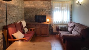 Una sala de estar acogedora con una pared de piedra, muebles de madera, un televisor y una ventana con cortinas.