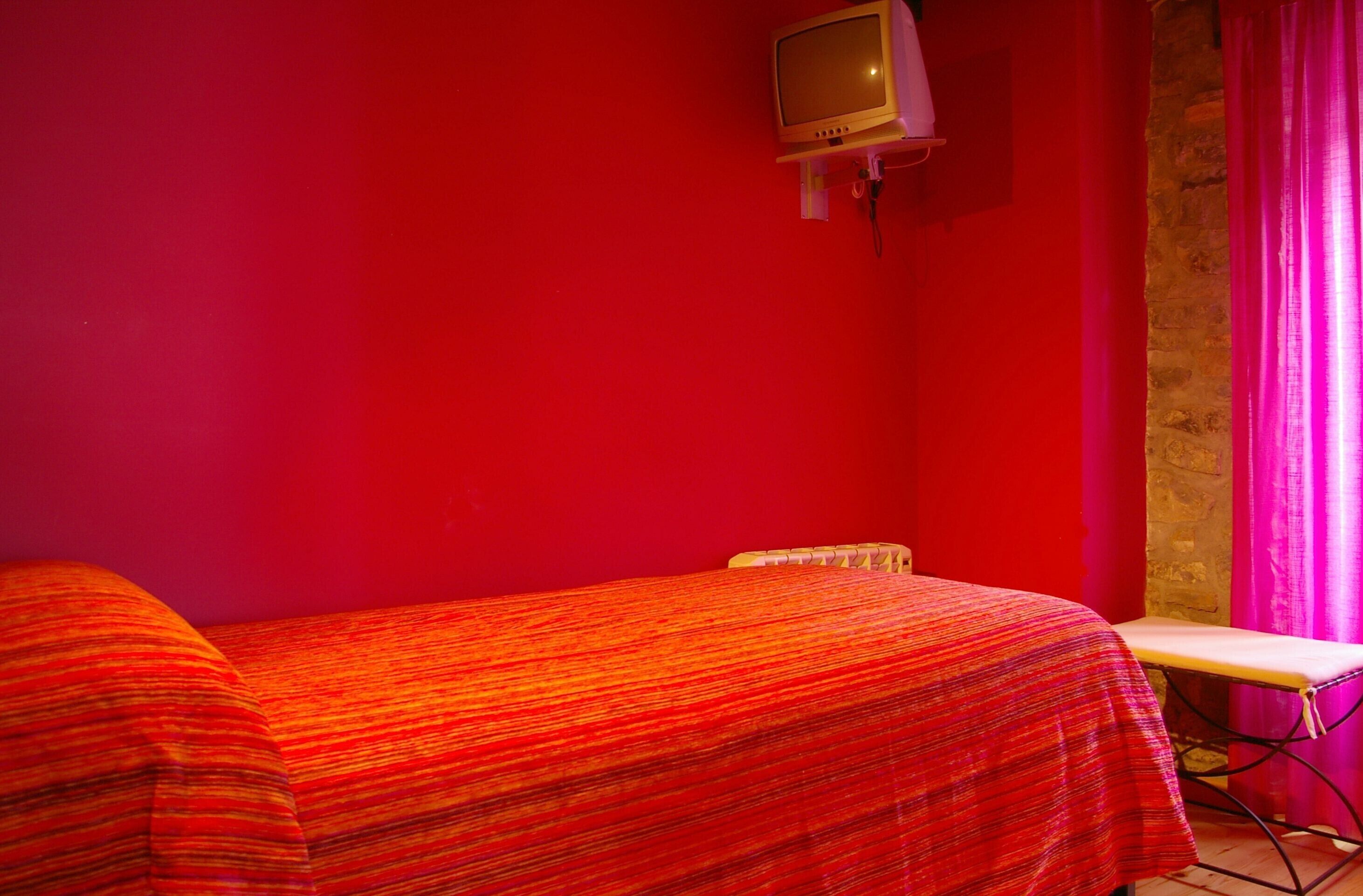 Ein Zimmer mit einem Bett, einem kleinen Tisch und einem an der Wand befestigten Fernseher.