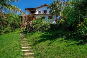 Ein weißes Gebäude mit Balkon, umgeben von üppiger Vegetation und einem gepflasterten Weg zum Eingang.