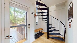 A spiral staircase with a black metal railing, a wooden bench, and a door leading outside. - Skyleaf A5 • Bright Mountain Escape (Sugar Mountain)