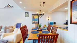 A dining area with a wooden table, chairs, a chandelier, and a poster on the wall. - Skyleaf A5 • Bright Mountain Escape (Sugar Mountain)