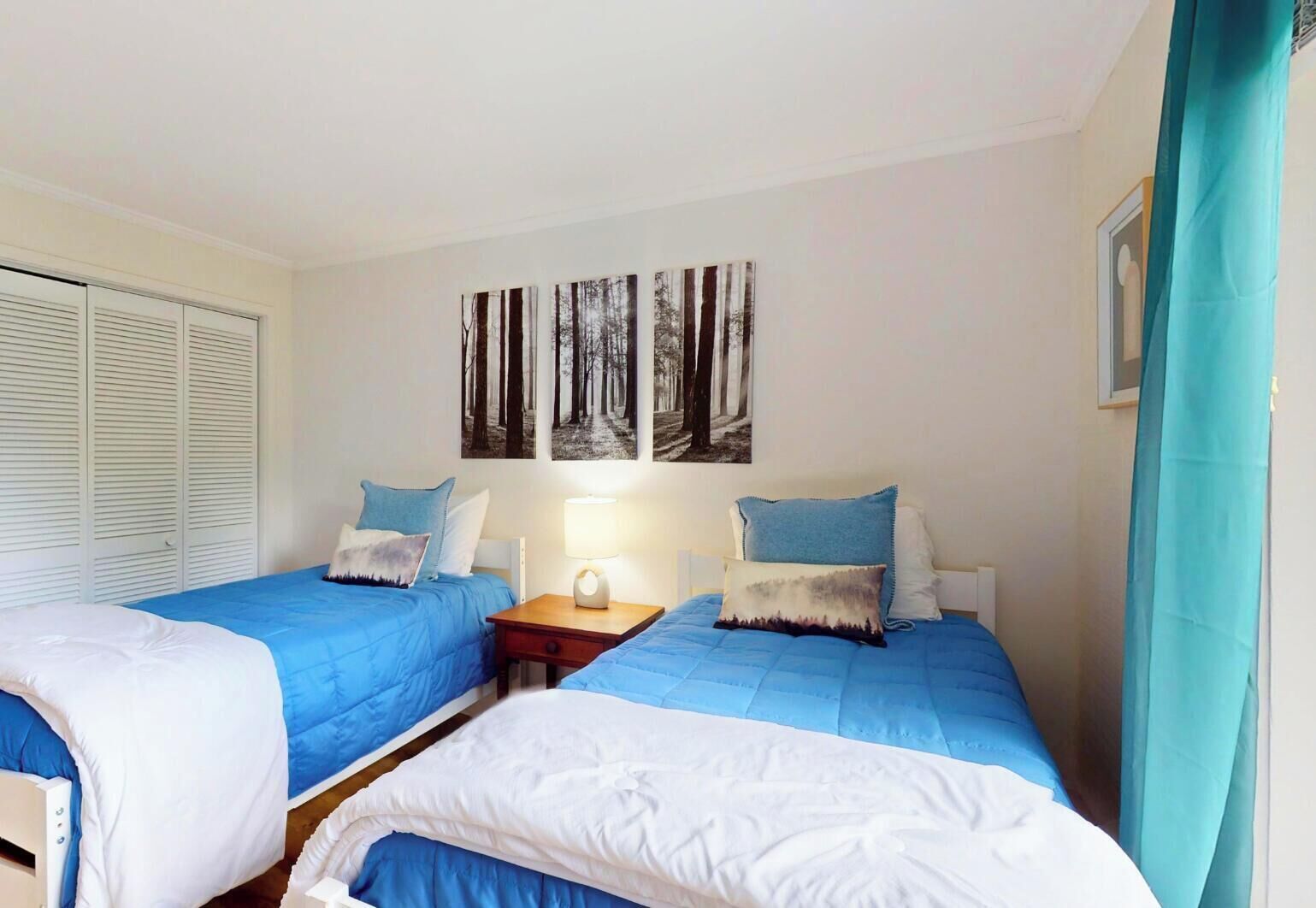 A room with two beds, a nightstand, and a wall with three forest-themed paintings.