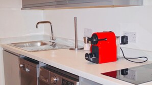 Una cocina con un lavaplatos de acero inoxidable, una cafetera roja y un lavavajillas.