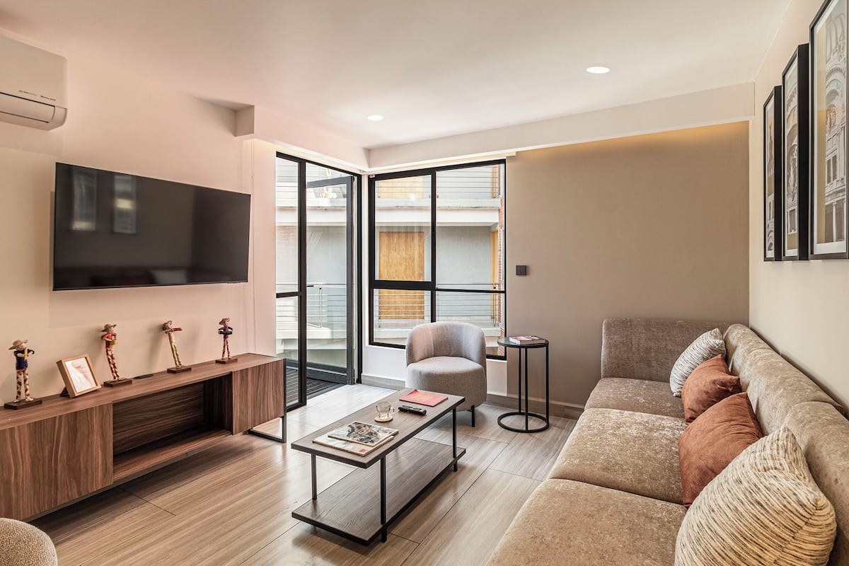 Una sala de estar moderna con una televisión de pantalla plana, un sofá, una mesa de centro y una silla.
