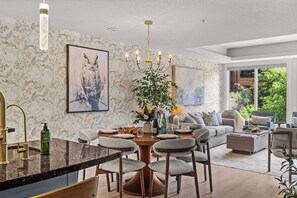 Een moderne woonkamer met een eethoek, een kroonluchter en kunstwerken aan de muren.
