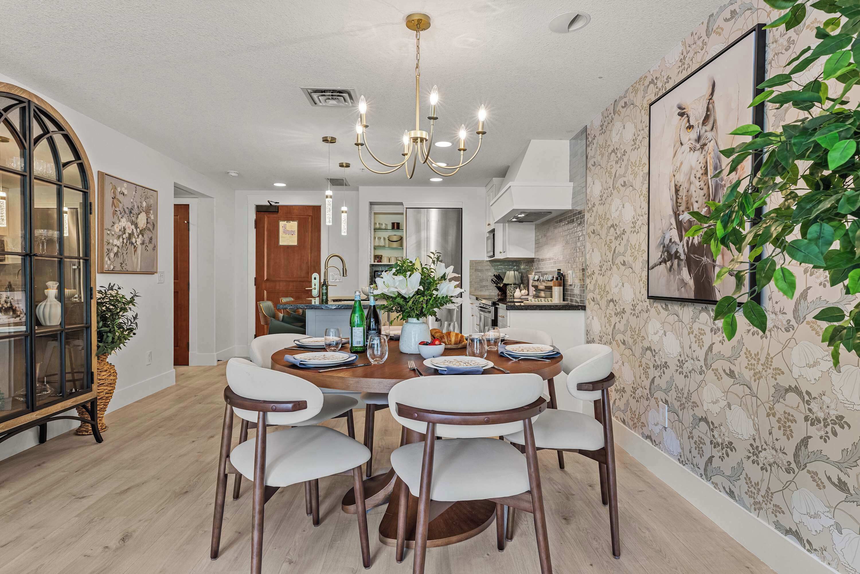 A dining area with a chandelier, a dining table set for six, and a wall with a floral wallpaper.
