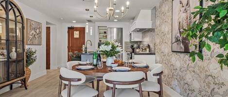 A dining area with a chandelier, a dining table set for six, and a wall with a floral wallpaper.