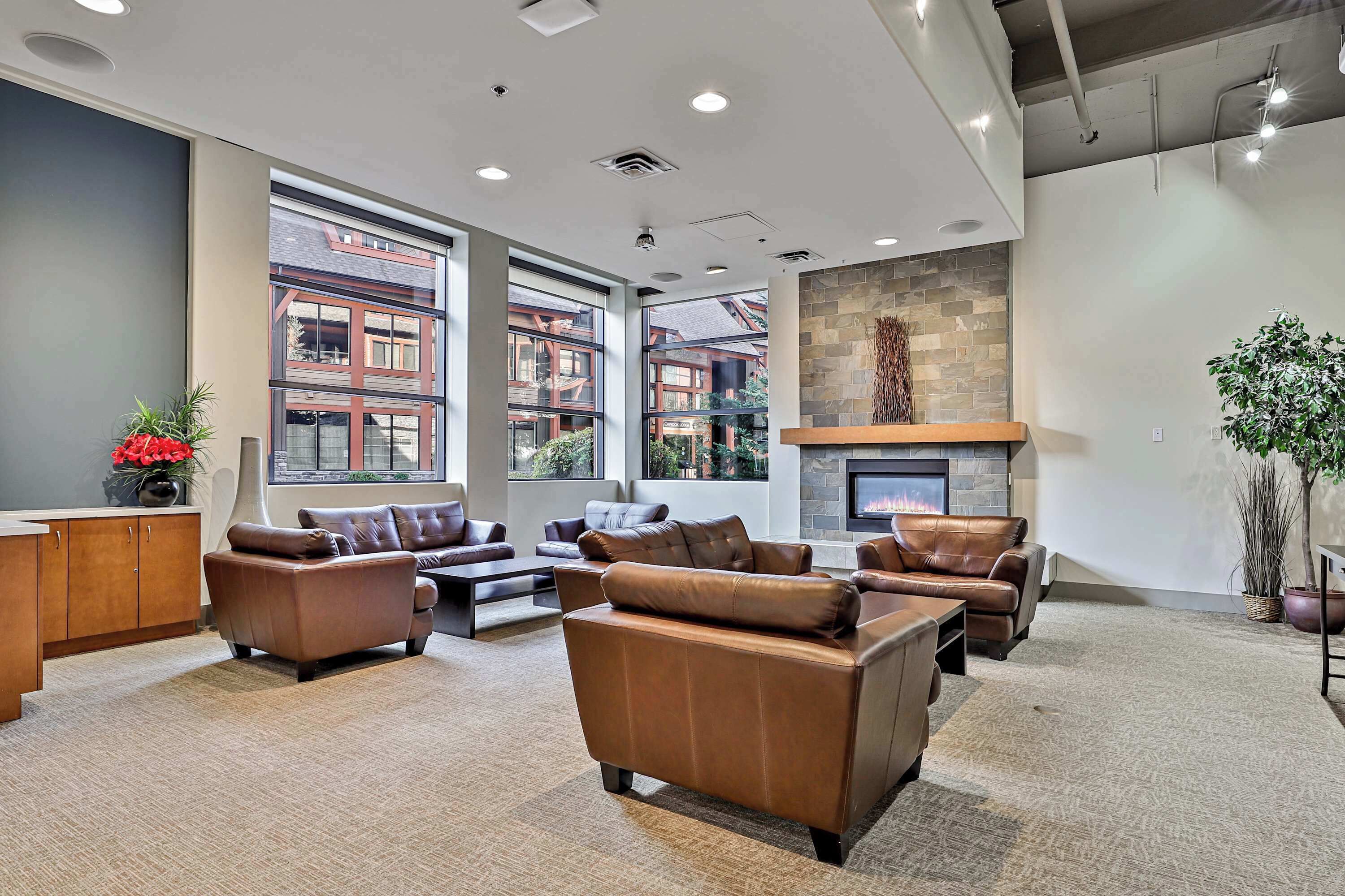 A spacious lounge area with leather sofas, a fireplace, large windows, and a stone accent wall.