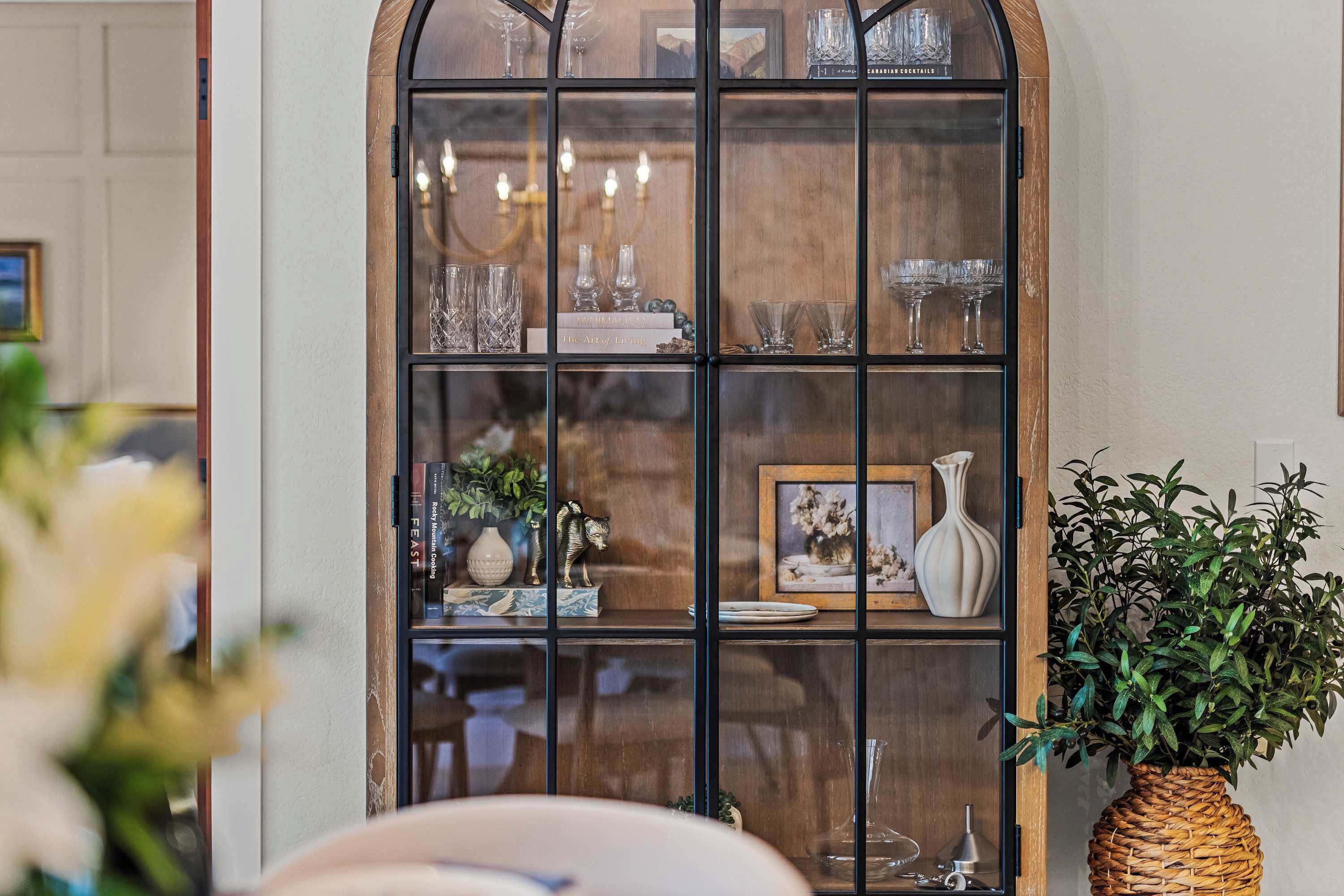 A wooden display cabinet with glass doors, containing various glassware and decorative items.
