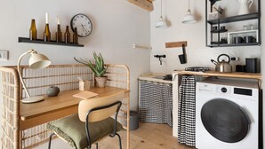Une cuisine de taille réduite avec une table en bois, une chaise, une horloge, une plante en pot et un lave-linge.
