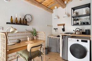 A compact kitchen with a wooden table, a chair, a clock, a potted plant, and a washing machine.
