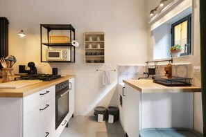 Kompakti keittiö, jossa on mikroaaltouuni, liesi ja säilytystilaa tarjoavat hyllyt.