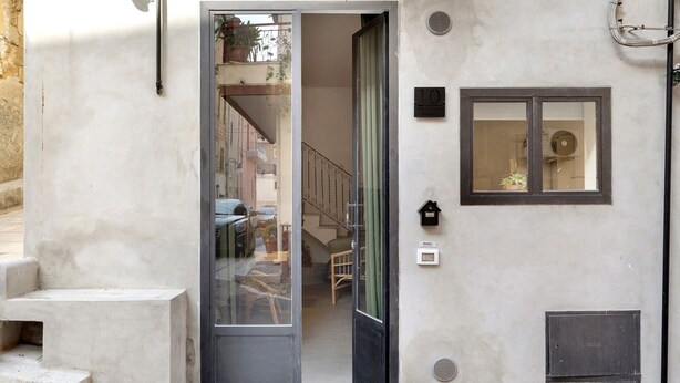 Une entrée étroite avec une porte vitrée donnant sur un escalier et une petite fenêtre ornée d’une plante.