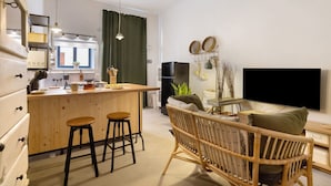 Une cuisine moderne avec des tabourets de bar en bois, un coin repas avec une chaise en osier et un téléviseur à écran plat fixé au mur.