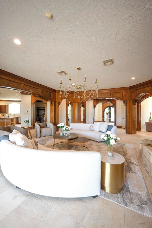 Ein geräumiges Wohnzimmer mit einer gebogenen weißen Couch, einem runden Couchtisch und einer Chandelier.
