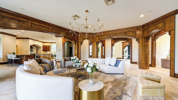 A spacious living area with a large chandelier, white sofas, and a gold coffee table.