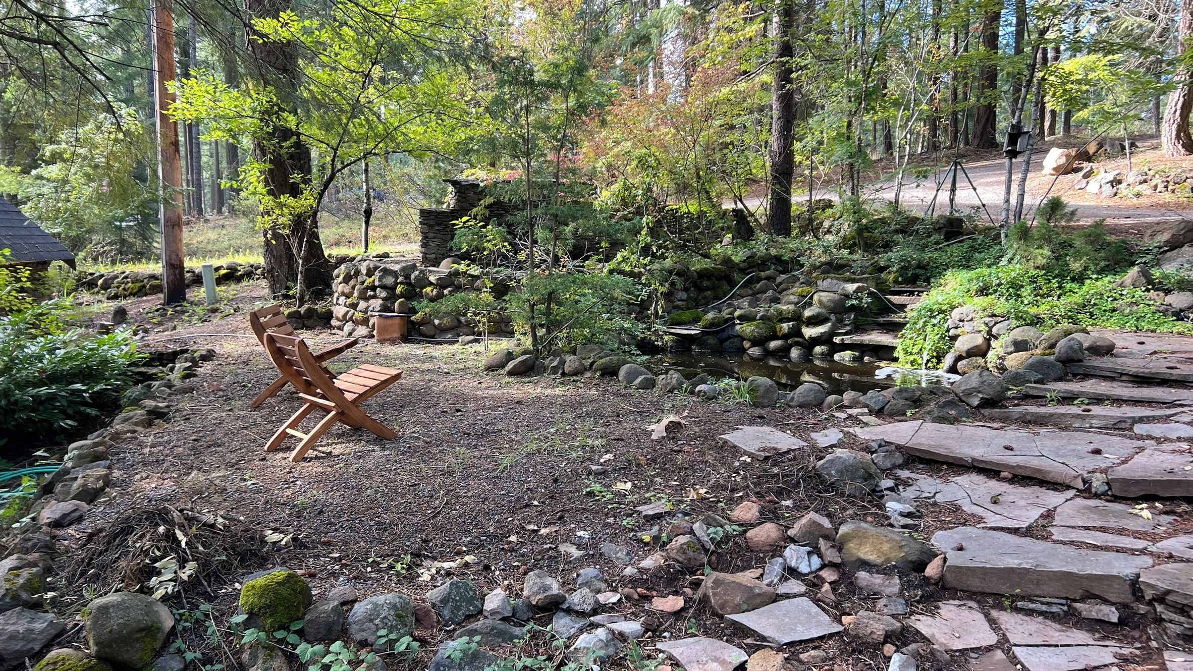 Un espace extérieur rustique aménagé avec un banc en bois, entouré d’un jardin composé de pierres naturelles et de rochers.