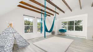 Una habitació àmplia amb grans finestres, cadira de balançament, sofà estampat i sostre de fusta.
