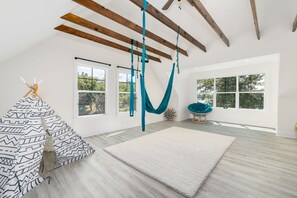 A spacious room with large windows, a hammock, a patterned sofa, and a wooden ceiling.