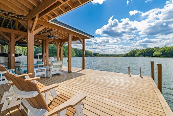 A wooden deck with chairs and a covered area overlooking a lake.
