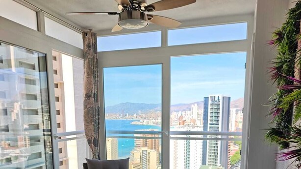 Ein Balkon mit Korbmöbeln, Deckenventilator und Blick auf die Stadt.