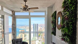 Eine hohe Wohnung mit Balkon, Deckenventilator, Sofa und Blick auf Stadt und Wasser.
