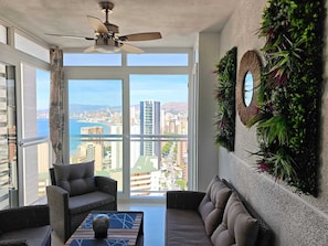 Eine hohe Wohnung mit Balkon, Deckenventilator, Sofa und Blick auf Stadt und Wasser.