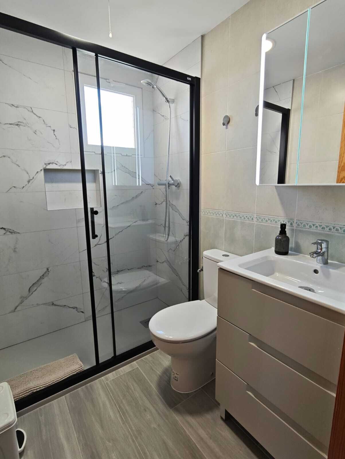 Un baño moderno con ducha acristalada, inodoro blanco y lavabo con espejo.