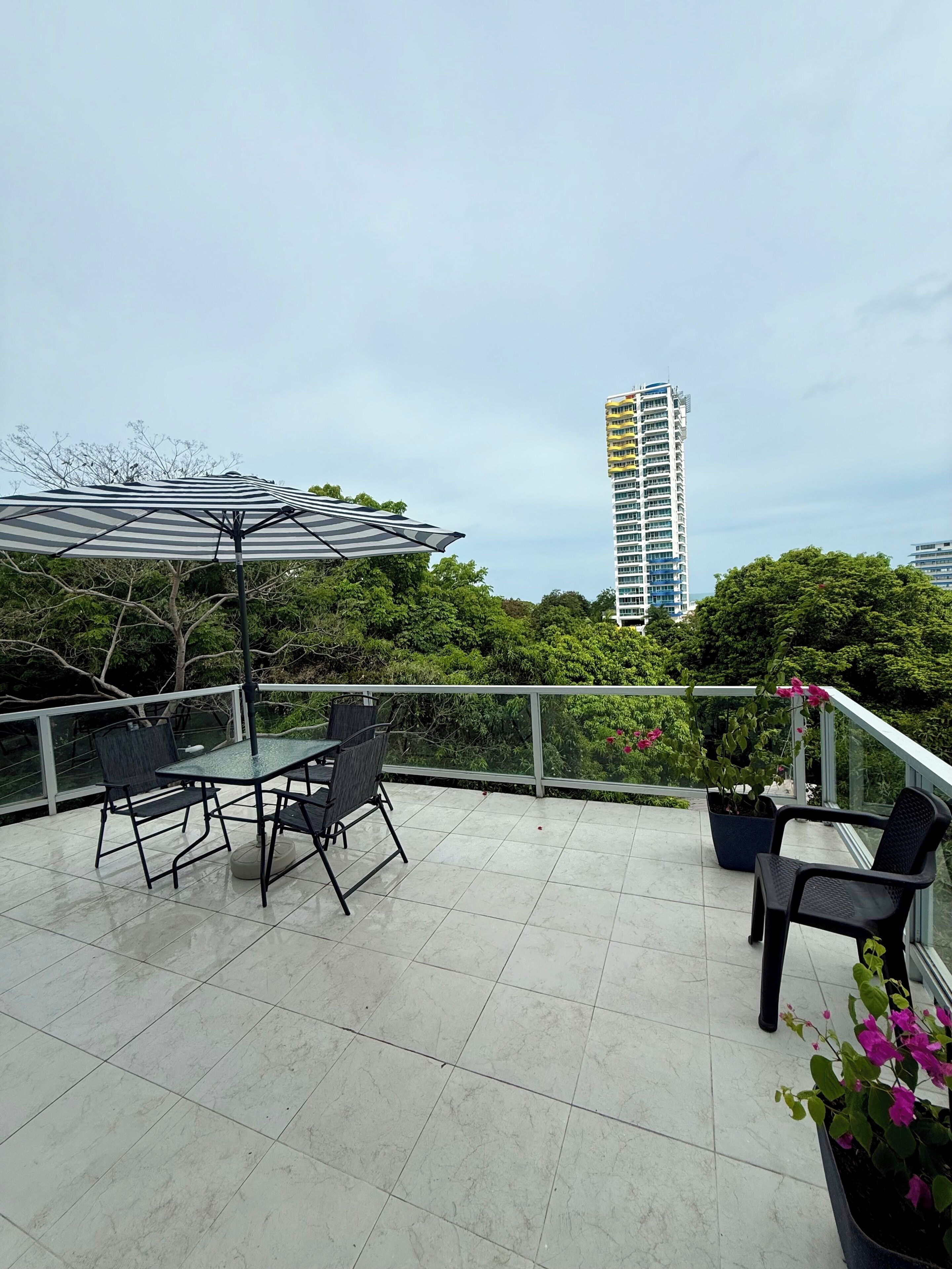 A rooftop terrace with a table and chairs, a striped umbrella, and potted plants.