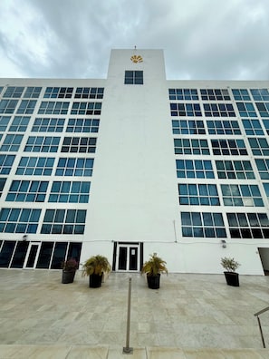 A large building with a central tower, multiple windows, and potted plants at the entrance.