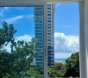 Un edificio alto con varios balcones, cielo despejado y exuberante vegetación en primer plano.