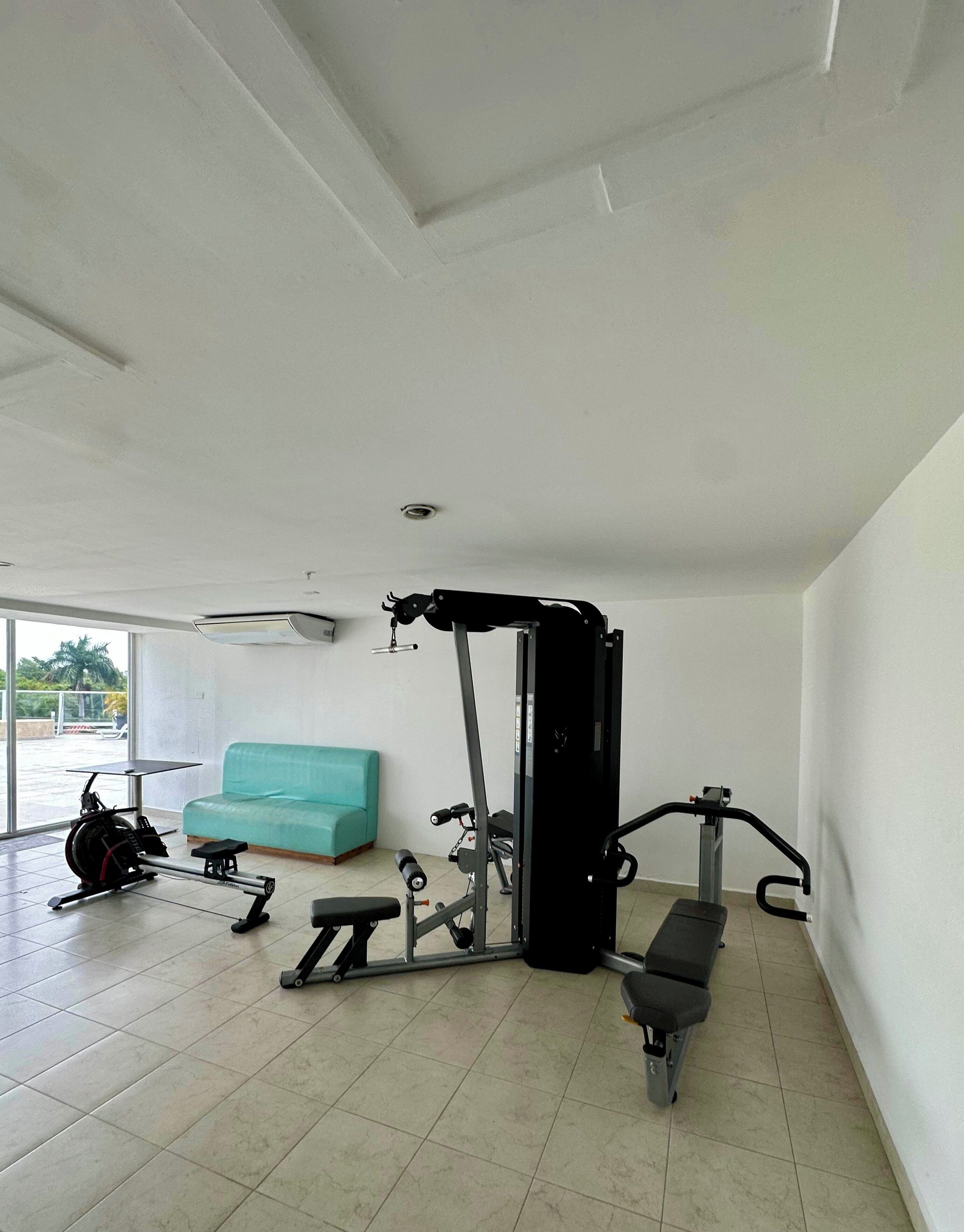 Een sportschool met trainingsapparatuur, een blauwgroene bank en een groot raam.