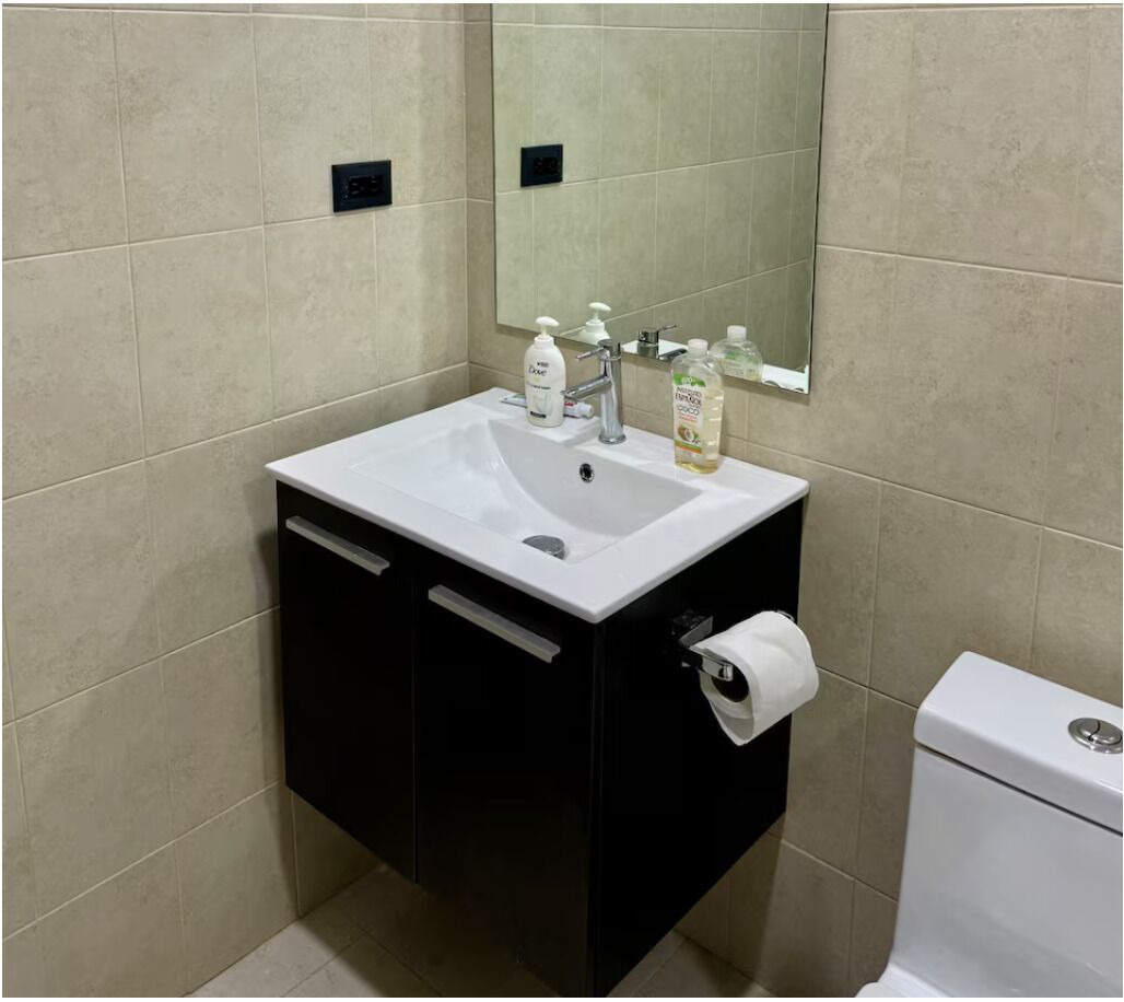 Un bagno con un lavandino bianco, un mobile contenitore nero e un water.