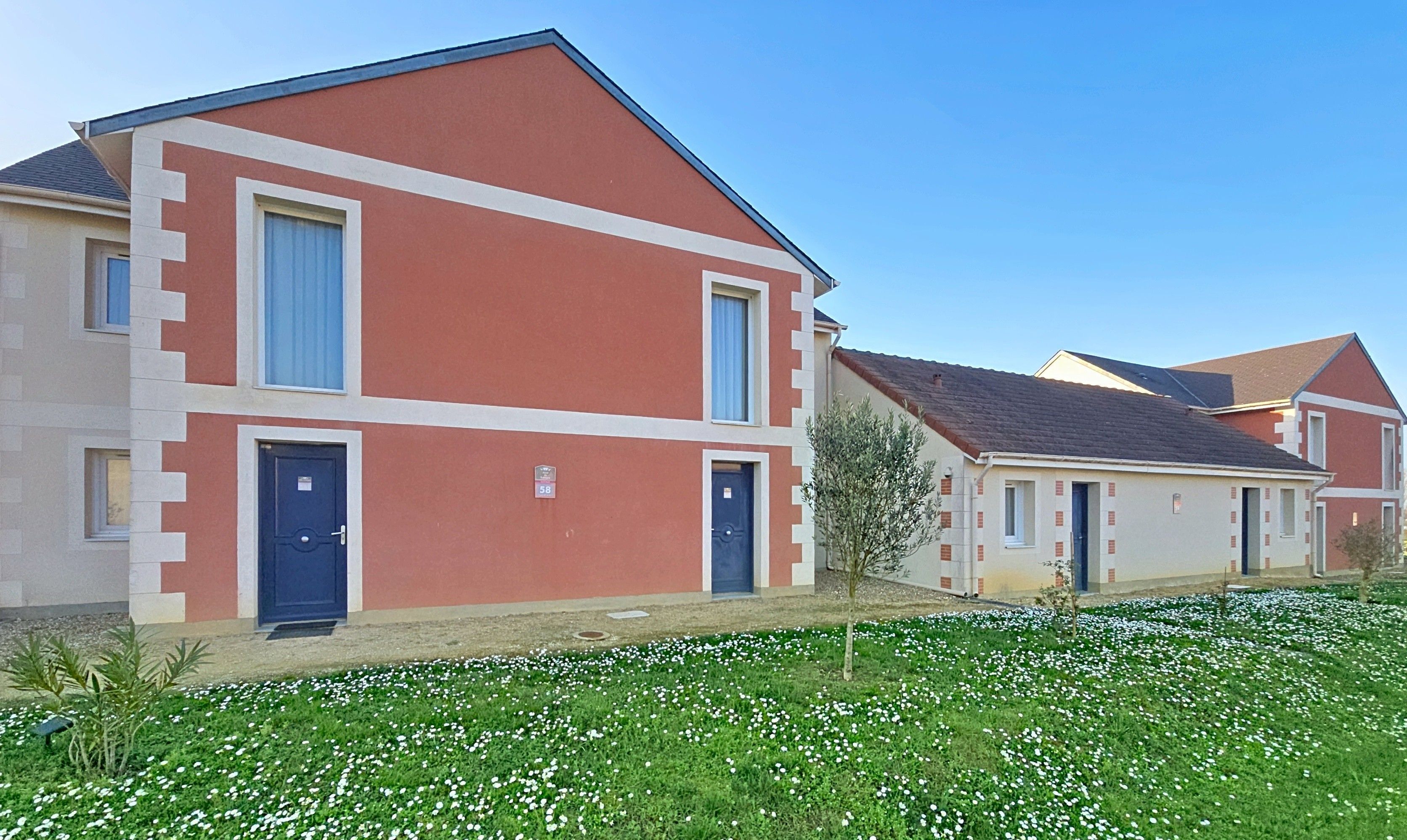Un immeuble d’habitation à la façade rouge, avec deux portes bleues et une enseigne portant le numéro « 58 ».