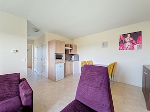 A modern apartment with a kitchen, dining area, and two purple armchairs.