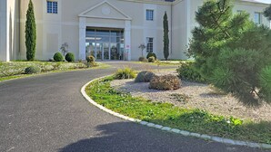 A building with a large entrance, a driveway, and landscaped areas with various plants. - Cosy studio près des châteaux de la Loire (Amboise)