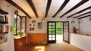 Een kamer met een houten bureau, boekenplanken, een stoel, een klein tafeltje, een raam en een deur die naar buiten leidt.