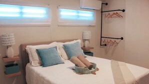 Una cama bien hecha con almohadas, una lámpara de noche, una cesta pequeña y un tendedero de pared.