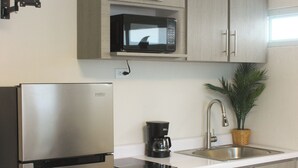 Una cocina con refrigerador de acero inoxidable, microondas, lavamanos y armarios de madera.