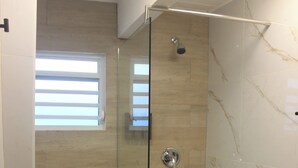 Un baño con ducha de vidrio, inodoro y un pequeño cubo de basura.