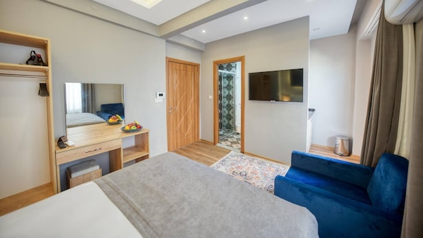 A modern hotel room with a bed, a desk with a mirror, a TV, and a blue sofa. - Taksim Square - Deluxe Studio 302 (Istanbul)