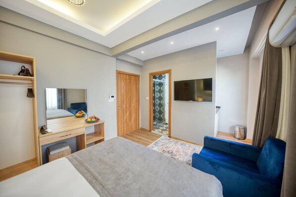 A modern hotel room with a bed, a desk with a mirror, a TV, and a blue sofa. - Taksim Square - Deluxe Studio 302 (Istanbul)