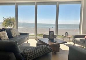Ein modernes Wohnzimmer mit großem Fenster mit Meerblick, einer Couch, einem Couchtisch und einem kleinen Beistelltisch.