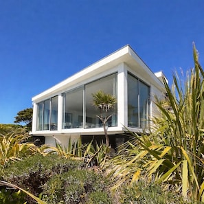Ein modernes Haus mit großen Fenstern, umgeben von heimischer Vegetation.