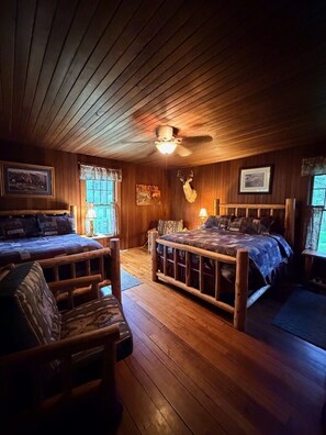 A cabin with two beds, a ceiling fan, wooden walls, and a mounted deer head.
